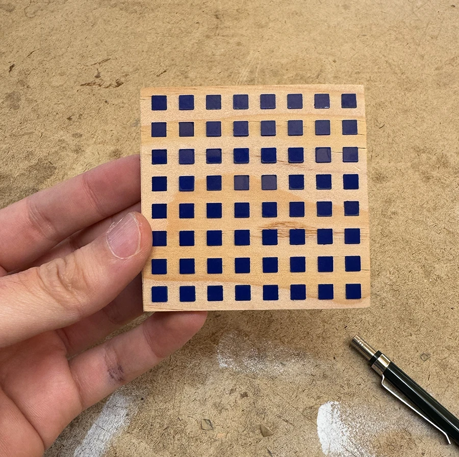 Small wooden piece with a grid of 8 by 8 squares filled in by acrylic squares. Small cracks are visible on the sides.
