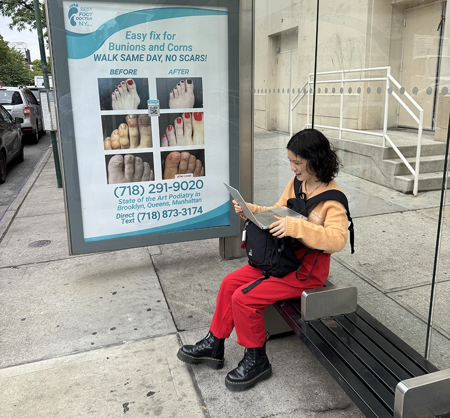 Person sitting down with a laptop in a bus stop.