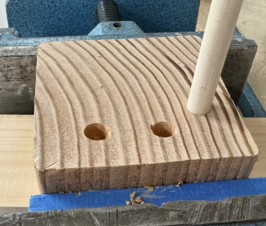 A small wood plant with 2 empty holes and a wooden dowel sticking out of a third hole.