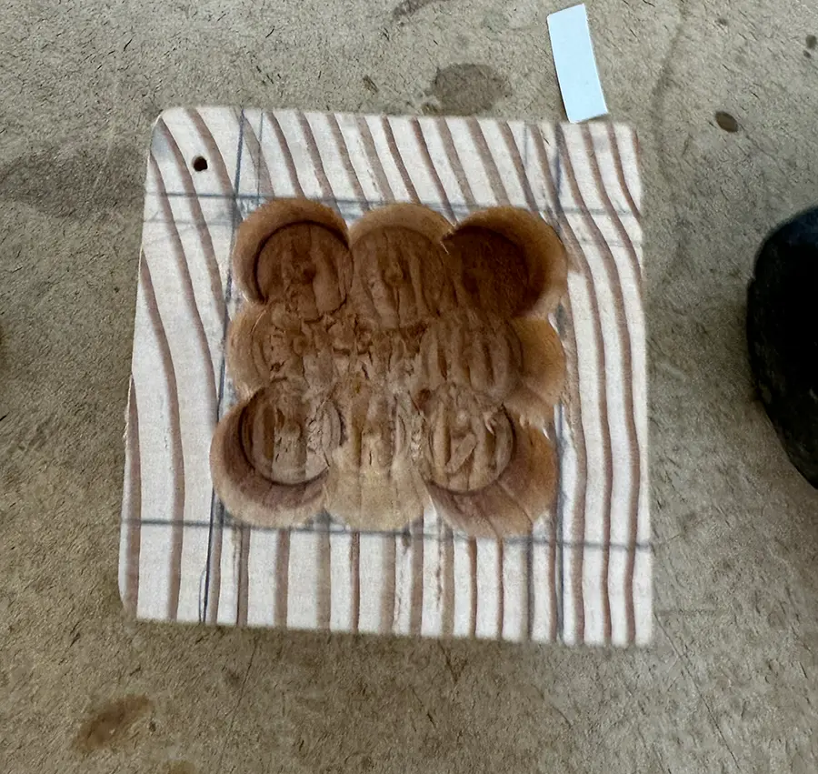 Top view of a wooden cube with a large rough cavity made of adjacent cilindrical holes.