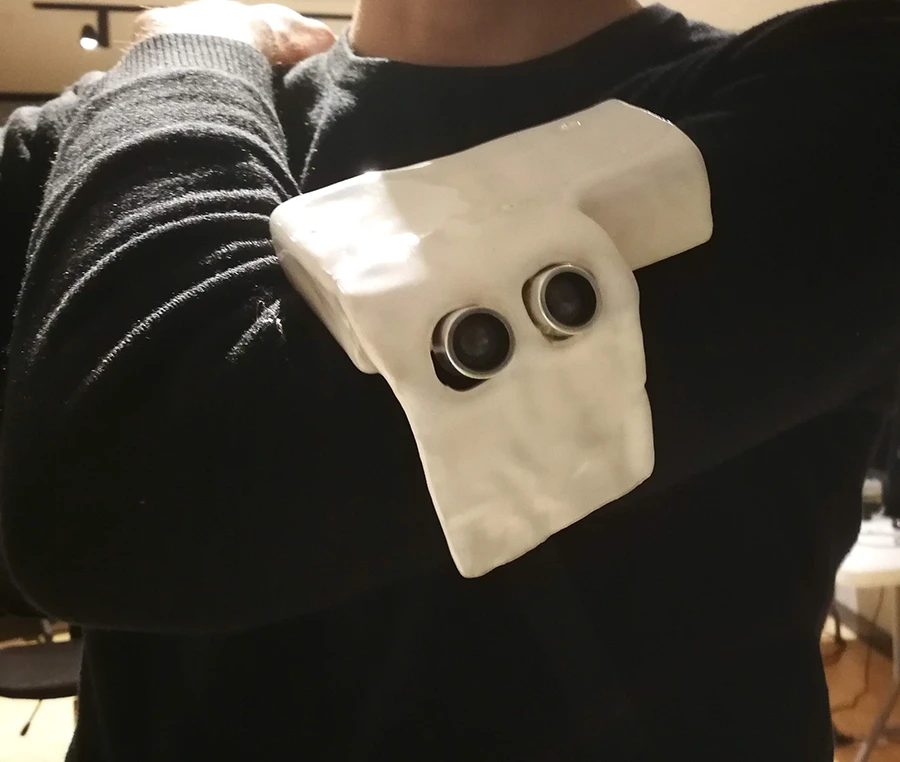 A small white ceramic object mounted on the upper portion of a man's arm, with two protruding ultrasonic transducers.