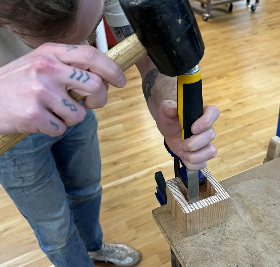 Wooden cube with a rough cavity being chiselled with a wood chisel and a rubber mallet.