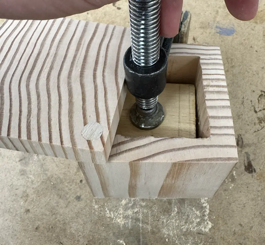 Small wooden box with a clamp holding a piece of wood inside it.