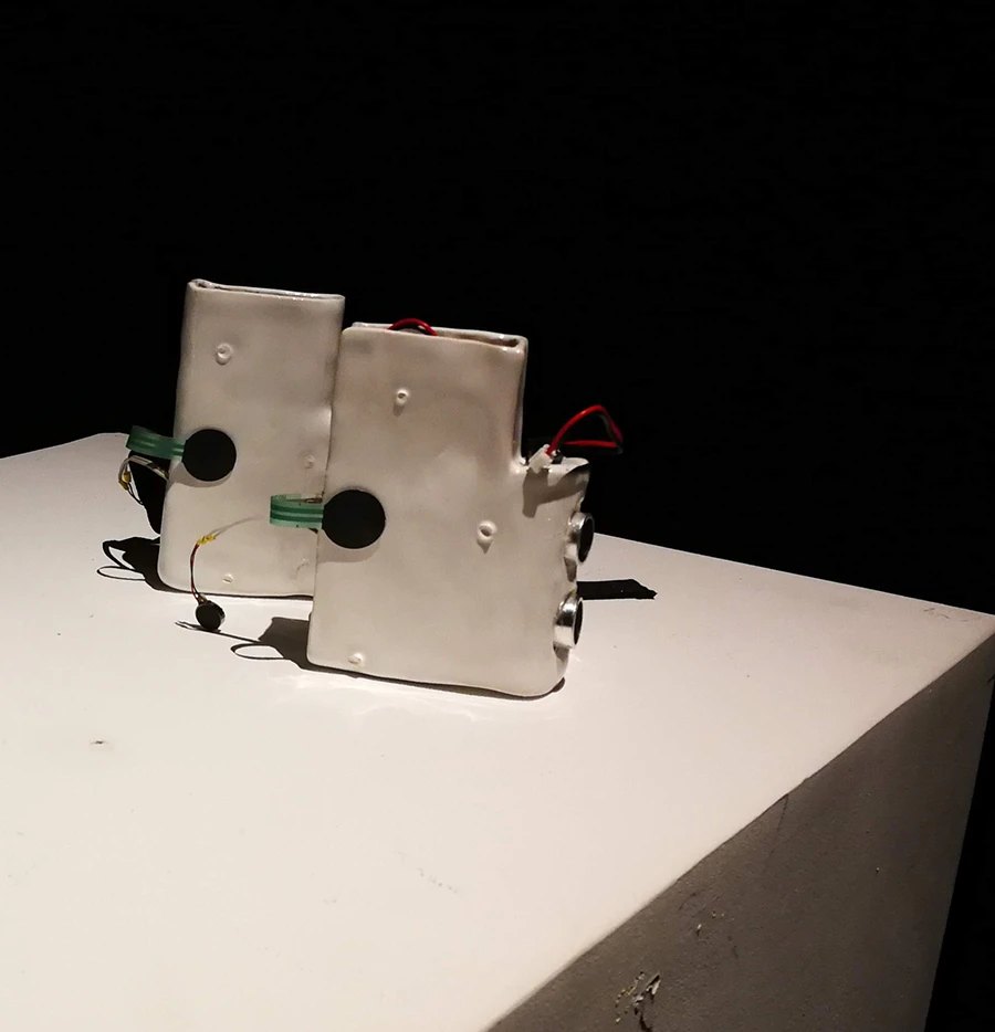 Two identical rectangular ceramic objects with protruding electronics, both on a white plinth over a black background.