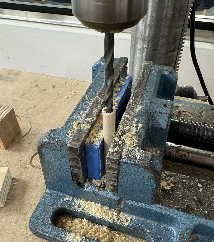 Bench drill drilling onto the top side of a dowel.