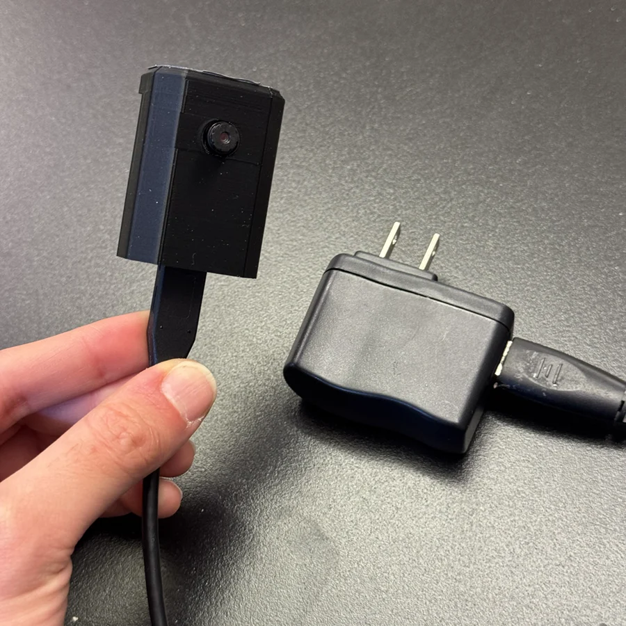 Black plastic camera connected to a two-prong plug adapter.