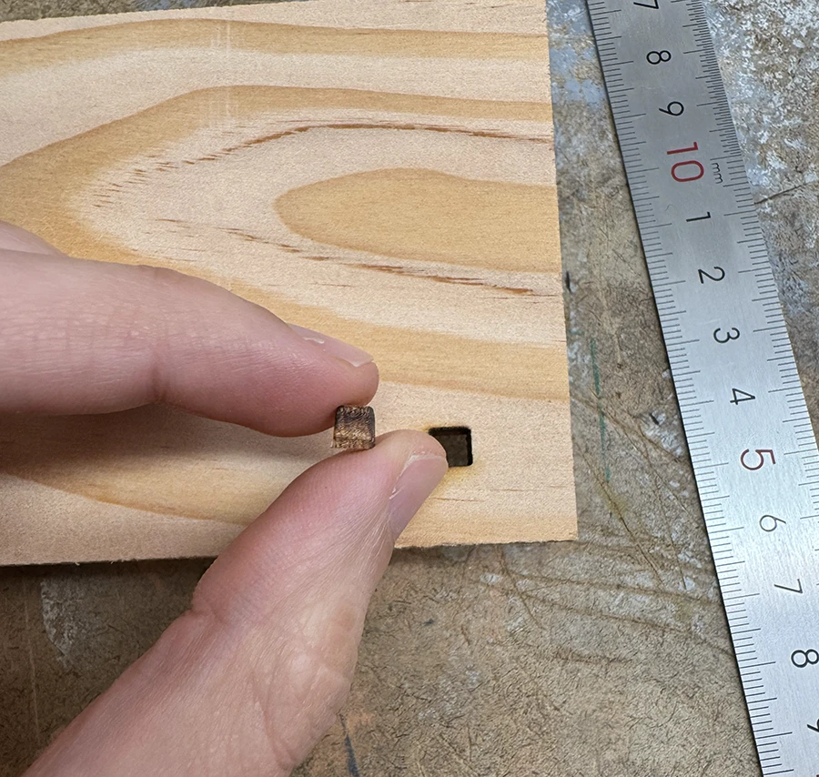 Wood plank with a square hole cut out. A hand hold the cut out piece.