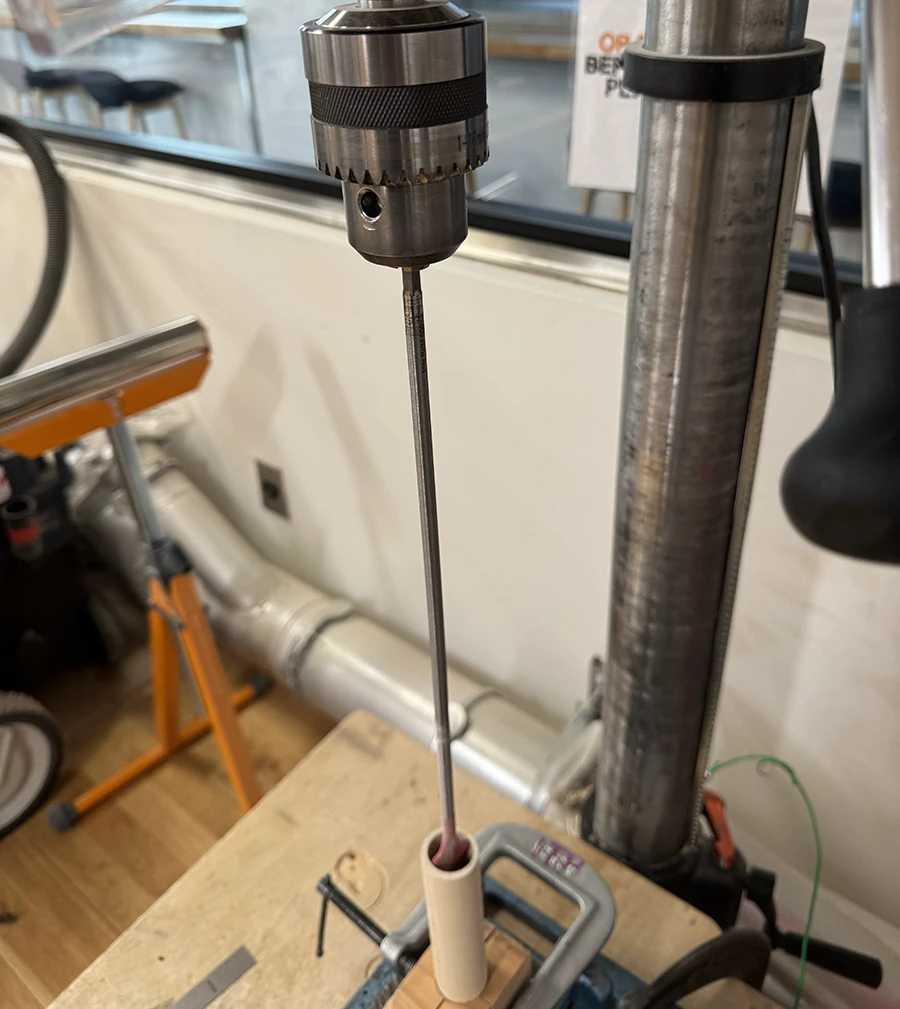Long spade bit mounted on the bench press over a dowel clamped down lengthwise.