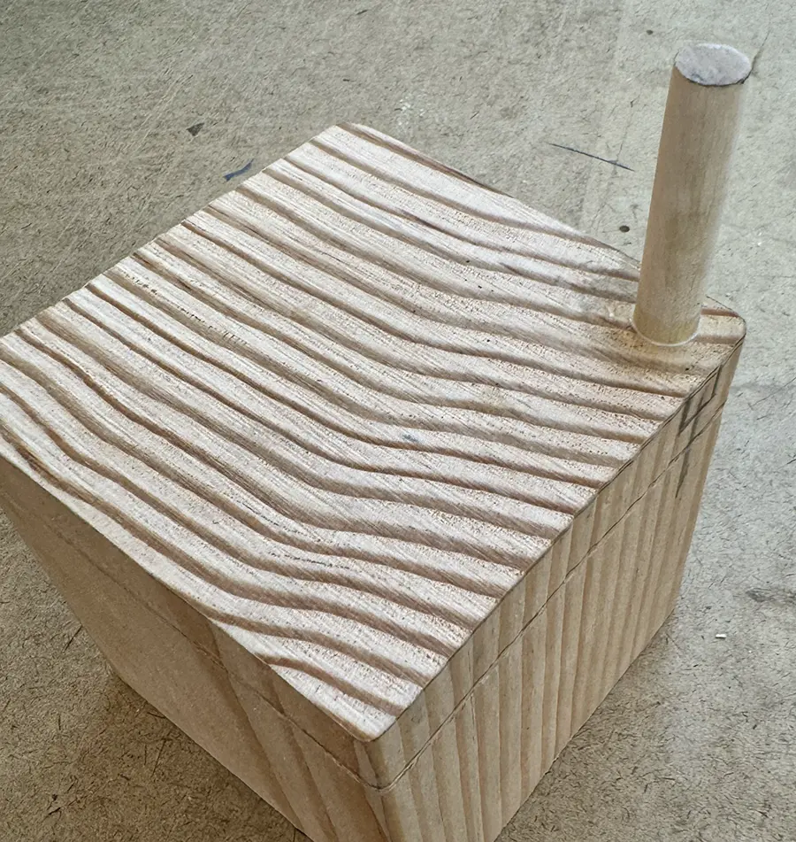 Wooden cube with a dowel sticking out of its top-right corner.