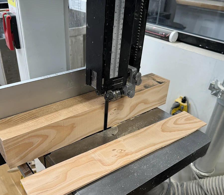 Large block of wood on the band saw with a slice taken off.