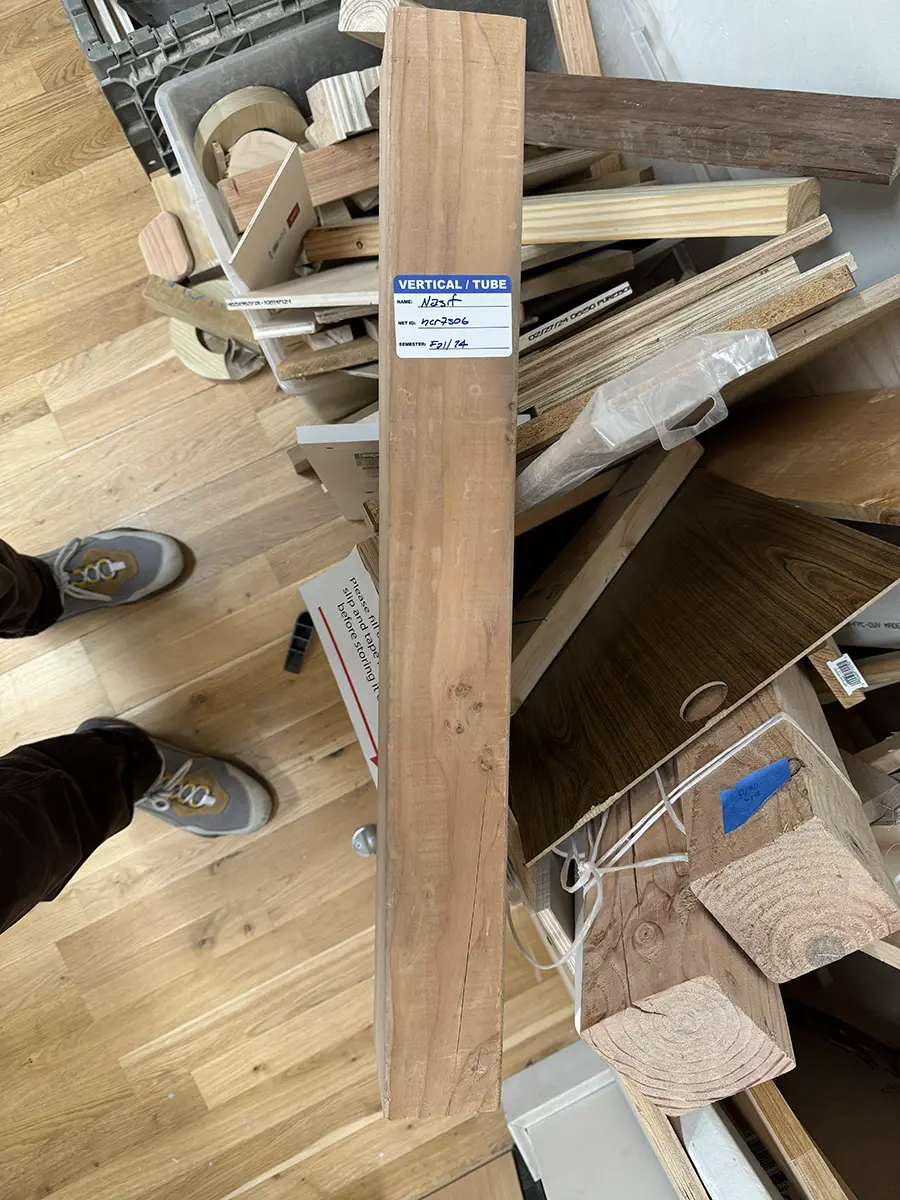 A long block of wood. A tag stuck on it reads 'Vertical/Tube' and contact details.