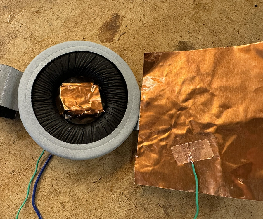 Soft switch built with two copper plates and a headphone piece foam in between. It is opened up, showing a crumpled up piece of copper inside the middle hole of the foam piece.