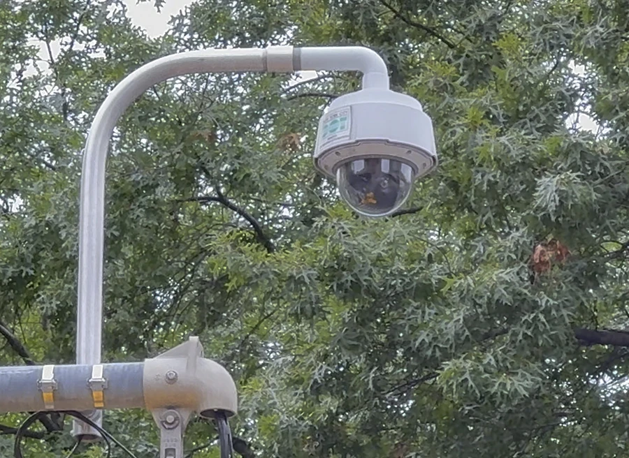 Photo of a traffic camera on top of a traffic light.