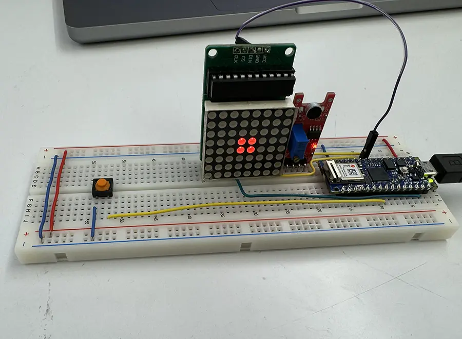 A circuit on a breadboard consisting of an arduino nano, a sound sensor, an LED 64 pixel screen and a small push button.